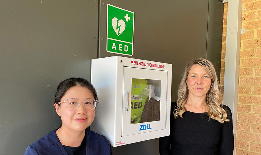 two women standing next to an AED mounted on a wall two women standing next to an AED mounted on a wall
